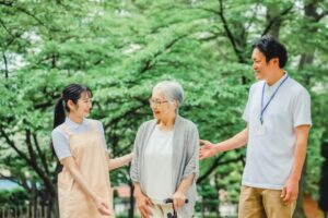 緑に囲まれた屋外で、スタッフと入居者が一緒に散歩・交流している風景